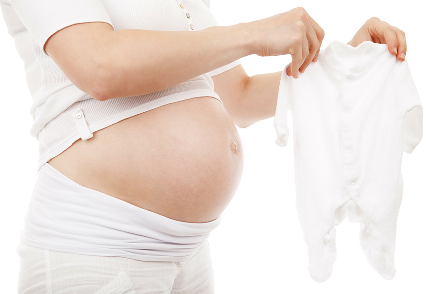 Pregnant person holding white baby clothes