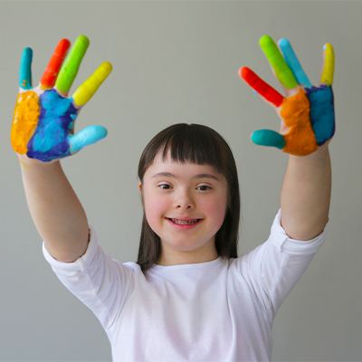 Young girl with Down syndrome holding up hands covered in paint