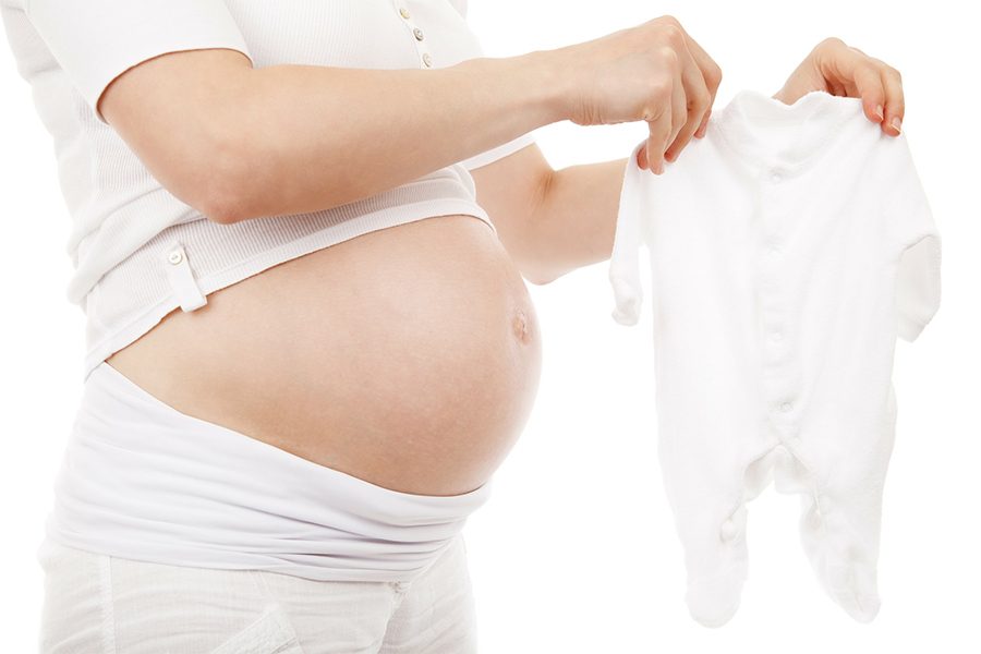 Pregnant person holding white baby clothes